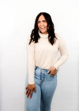 Load image into Gallery viewer, model wearing the by your side top in the color cream paired with a pair of lightwash denim. model is standing with one hand in her pocket with her thumb through a belt loop and the other hand resting on her thigh. model is smiling and looking to the side.