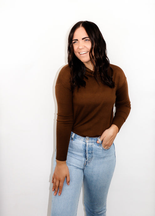 model wearing the by your side top in the color espresso paired with a pair of lightwash denim. model is standing with one hand in her pocket with her thumb through a belt loop and the other hand resting on her thigh. model is smiling and looking out past the camera.