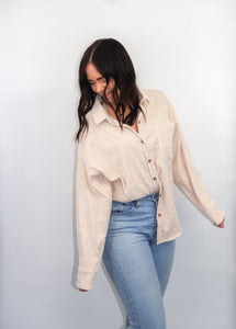 model wearing the anywhere but here lightweight corduroy shacket in the color sand. model has paired the top with a pair of light denim and is smiling and looking downward.