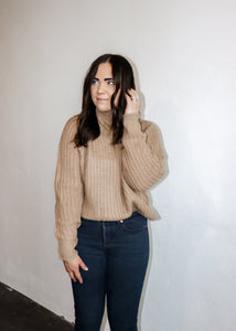 model wearing the patiently waiting sweater in the color oat. model has the sweater paired with a pair of black denim.
