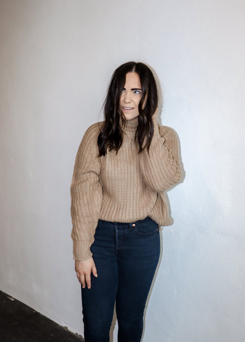 model wearing the patiently waiting sweater in the color oat. model has the sweater paired with a pair of black denim.