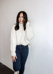 model wearing the patiently waiting sweater in the color ivory. model has the sweater paired with a pair of black denim.