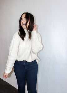 model wearing the patiently waiting sweater in the color ivory. model has the sweater paired with a pair of black denim.