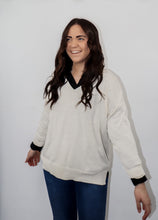 Load image into Gallery viewer, model wearing the state of grace sweater in the color cream. model has the sweater paired with the play by my rules top in the color black and a pair of high-waisted dark-wash denim.