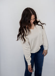 model wearing the state of grace sweater in the color cream. model has the sweater paired with a pair of high-waisted dark-wash denim.