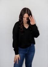 Load image into Gallery viewer, model wearing the state of grace sweater in the color black. model has the sweater paired with a pair of high-waisted dark-wash denim.