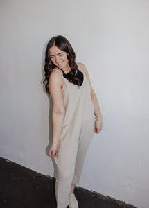 model wearing the never felt this way jumpsuit in the color parchment. model hs the jumpsuit paaired with the these days top in the color black and a pair of platform sneakers.