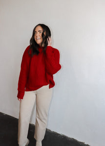model wearing the patiently waiting sweater in the color red. model has the sweater paired with the siena denim.