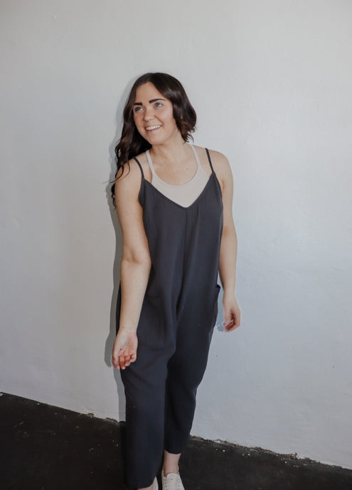 model wearing the never felt this way jumpsuit in the color washed black. model has the jumpsuit paired with the these days top in the color chalk and a pair of platform sneakers.