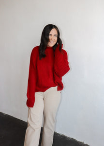 model wearing the patiently waiting sweater in the color red. model has the sweater paired with the siena denim.